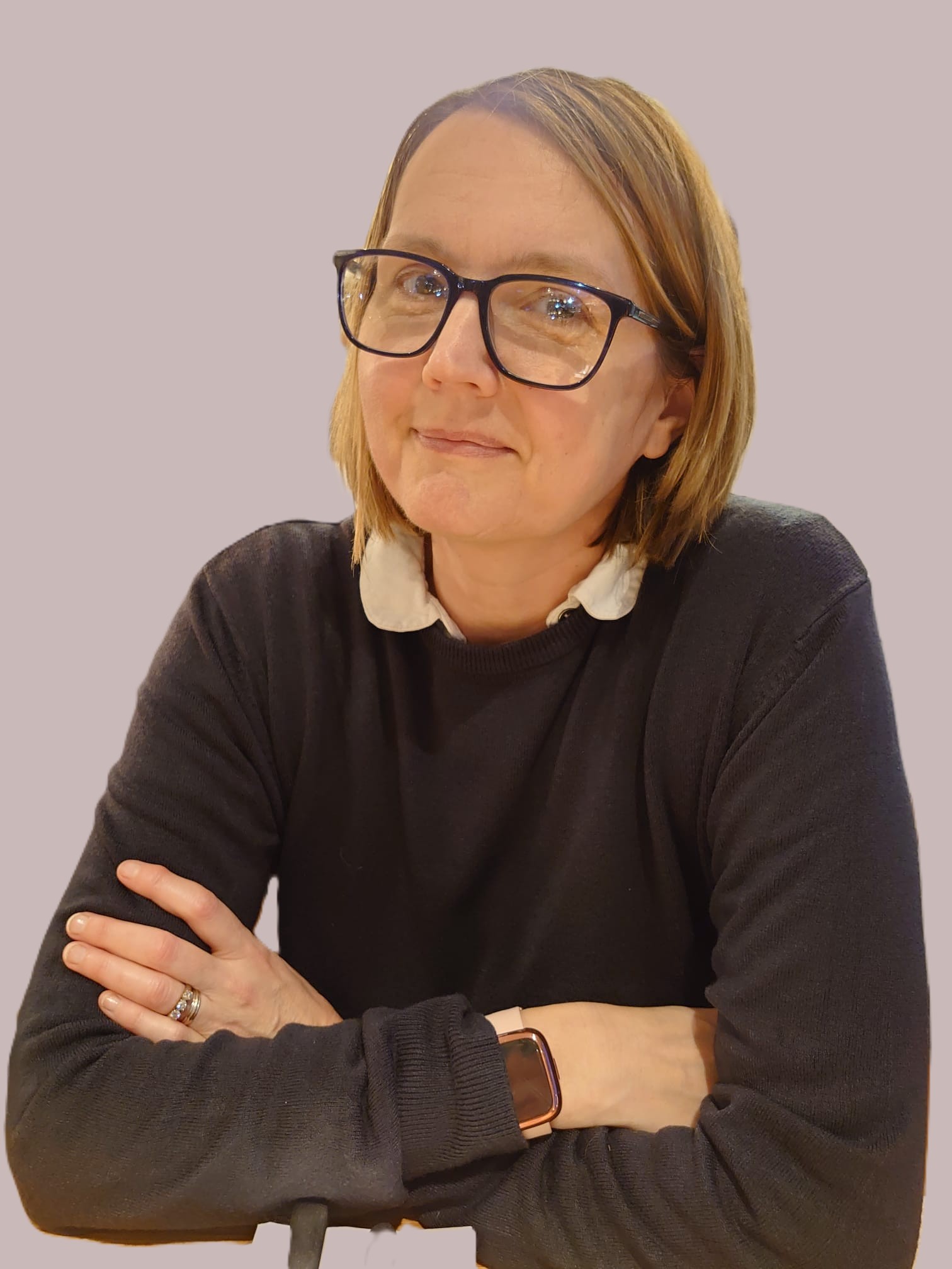 The photo shows me, Florence Morimont in a seated position with my arms crossed casually in a relaxed manner.  I am a white woman with light coloured near shoulder length hair.  I am wearing blue rimmed glasses, a white blouse and a blue jumper.
