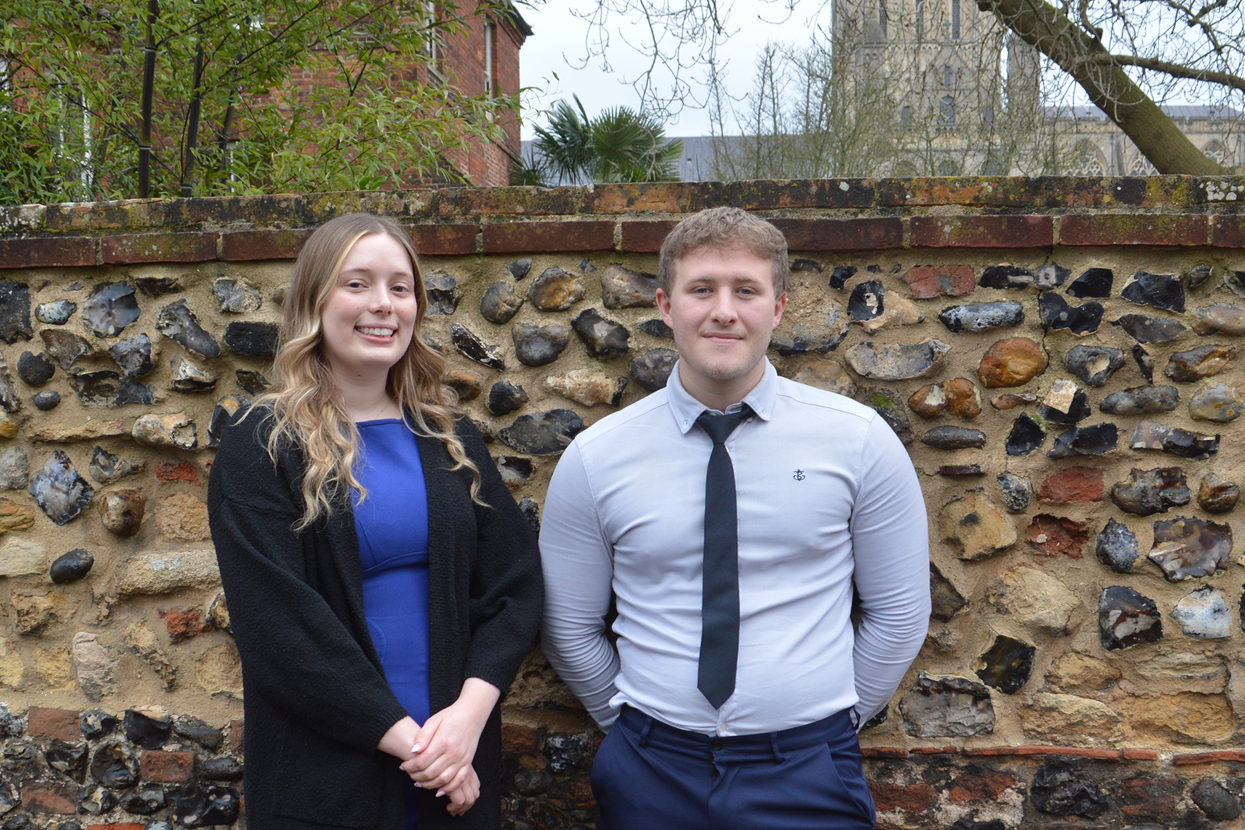 Lauren Yates and Kieran Flood smiling at the camera in the Cathedral Close.