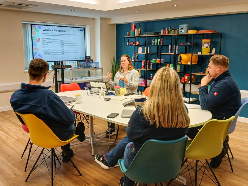 Photo of a small classroom with adults sat around a round central table. 